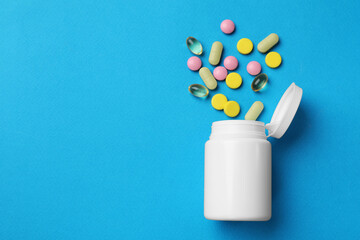 Different vitamin pills and bottle on light blue background, top view. Space for text