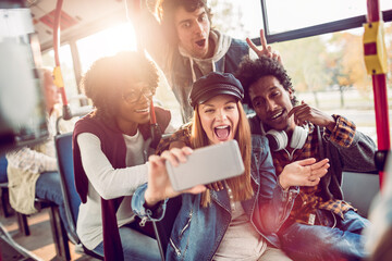 Group of happy young friends taking a selfie on a city bus