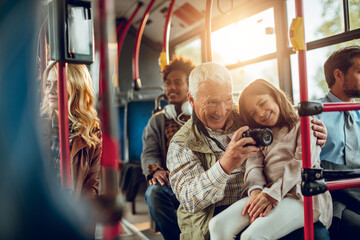 Grandfather and granddaughter taking pictures on city bus with passengers