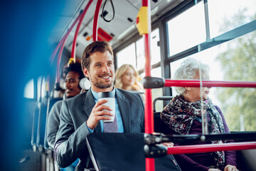 Smiling young adult businessman drinking coffee on the bus