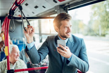 Smiling young adult businessman using smartphone on the bus