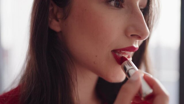 A beautiful woman in a close-up shot, applying red lipstick carefully at her cozy home setting.