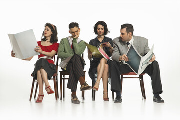 Group of four people, men and women in retro-style clothes sitting on chair and reading newspapers, journals on white background. Concept of retro and vintage, fashion,