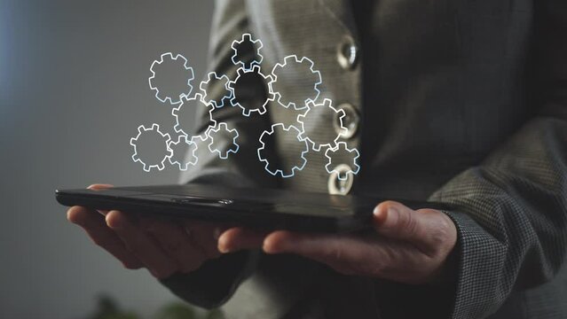 An animated background of rotating gears above the tablet screen in the hands of a businesswoman. Cg