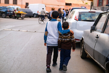 Two brothers walk down street, older one affectionately embracing younger, view from behind, family...