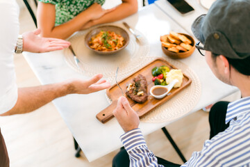 Waitress man serving food to group of diverse customer in restaurant, eatery client woman and man having smile and happy with service mind from cafes staff, lunch or dinner time lifestyle with family