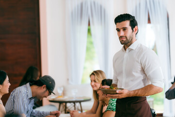Waitress man serving food to group of diverse customer in restaurant, eatery client woman and man having smile and happy with service mind from cafes staff, lunch or dinner time lifestyle with family