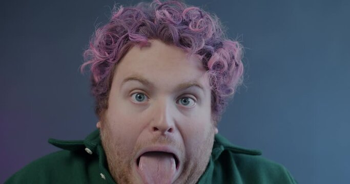 Close-up slow motion portrait of crazy young man screaming and making funny faces on purple background. Expression and emotion concept.