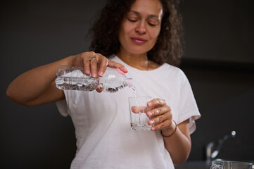 Focus on a bottle of fresh clean pure water in the hands of a woman pouring water into drinking...