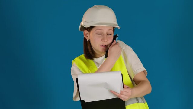 Lady laughs engaging in mobile phone conversation on blue background. Female builder has pleasant conversation with customer on smartphone