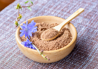 Ground chicory root on a wooden spoon and chicory flowers on a rustic wooden background. Alternative medicine. Healthy drinks. chicory drink