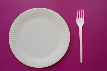 White paper plate with a plastic fork on a dark purple background, disposable dishes, simple serving of disposable dishes, close-up