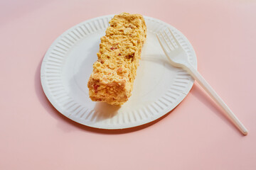 Creamy cake with nuts on a paper plate with a plastic fork on a pink background, nut dessert on disposable dishes, a portion of cake with nuts, dessert on disposable dishes