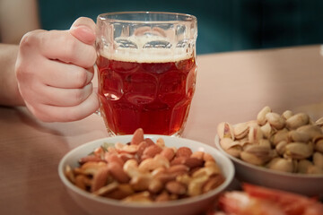 Hand taking a mug of beer on a table with nuts and shrimps, snacks for beer in a beer bar, close-up