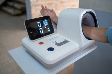 Medical care patient checking blood pressure on BP monitor machine with arm inserted into the...