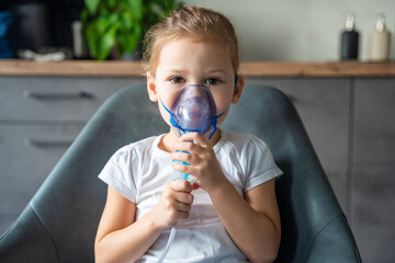 Cute little girl are sitting and holding a nebulizer mask leaning against the face, airway treatment concept - obrazy, fototapety, plakaty