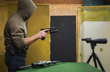 Tactical shooting at a shooting range, a man in a hood with a pistol in his hand.