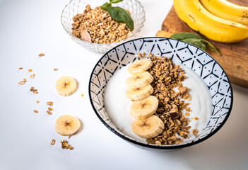 Breakfast bowl with yogurt, cereal and sliced ​​banana pieces with a glass bowl with cereal and two bananas around
