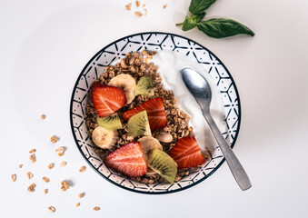Overhead view of a breakfast bowl with yogurt, cereal and pieces of kiwi, banana and sliced ​​strawberry with a spoon