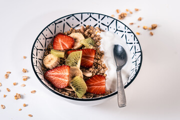 Breakfast bowl with natural yogurt and sliced pieces of strawberry, banana and kiwi with a metal spoon