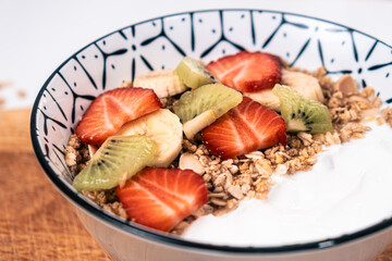 Breakfast bowl with natural yogurt, cereal, and sliced pieces of strawberries, banana and kiwi on a wooden board