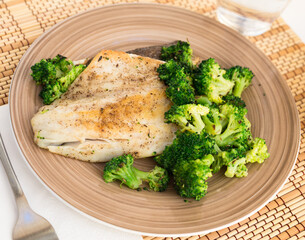 Fried fillet of sea bass with garnish of broccoli on black warm stone plate
