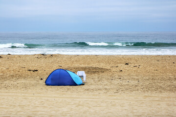 Blue sun shelter tent and chair at empty Pacific beach in the early hours of typical seaside gloomy morning, San Diego, California