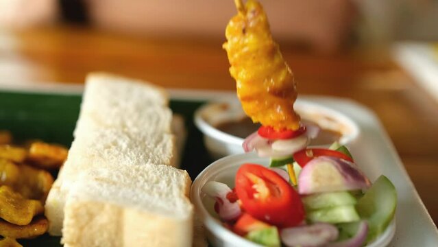 Pork satay skewers are dipped in pickles which are cucumber slices and onions in vinegar.