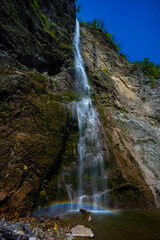 Waterfall hidden inside the forest, beauties of Slovenia to be discovered. Near Nova Gorica, Tolmin village. Water spray and vivid rainbow forms from the waterfall that falls sheer onto the rock.