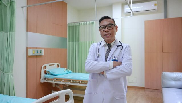 Asian middle-aged physician with stethoscope wearing lab coat uniform standing in patient room or clinic looking camera arm crossed smiling, doctor occupation working in hospital express happy feeling