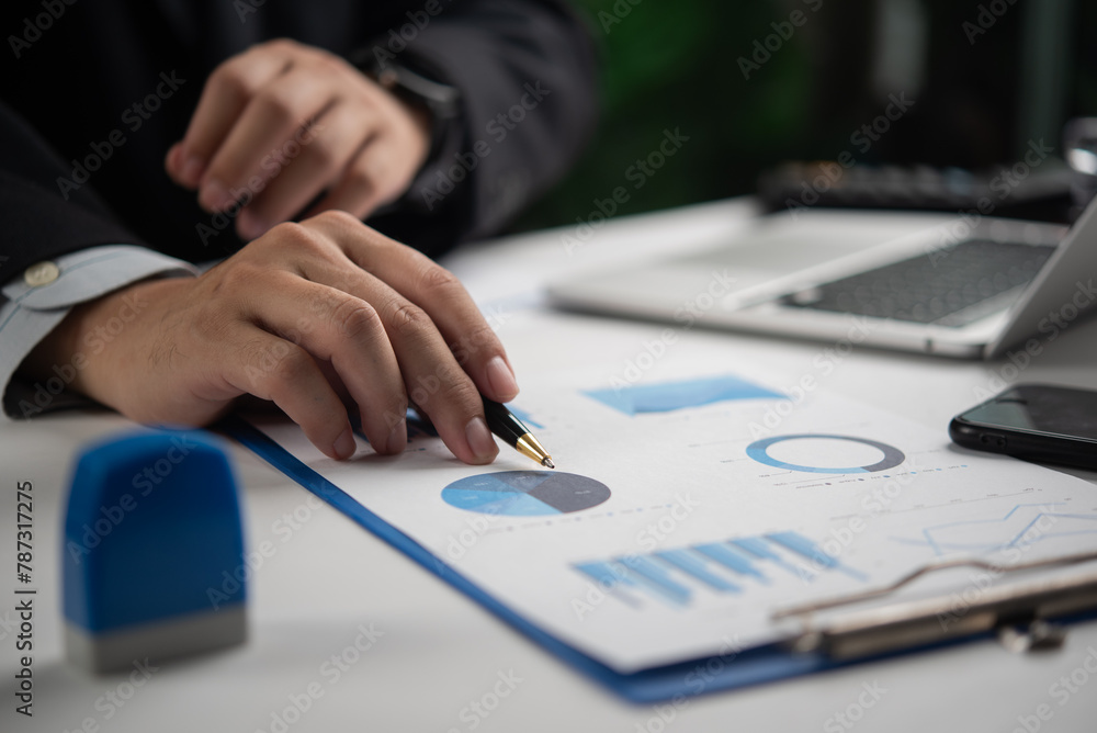 Poster businessman analyzing pie chart and graph data with pen on desk with laptop and smartphone