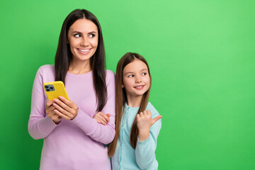 Portrait of two people hold smart phone look indicate finger empty space isolated on green color...