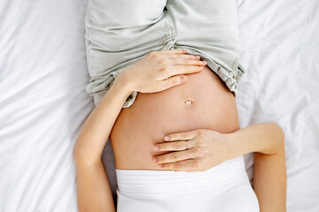 A pregnant woman in jeans with an open stomach strokes him with her hands. The future mother. The...
