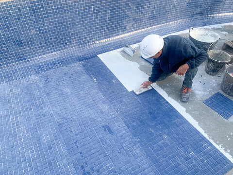 Operario de la construcci&oacute;n pavimentando con gresite azul una piscina en una obra de construcci&oacute;n 