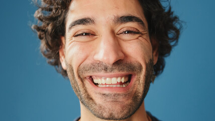 Close-up, man opens his eyes smiling and looking at camera isolated on blue background in studio