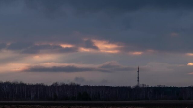 Burning clouds in sky with telecommunication tower silhouette. Evening timelapse of clouds floating in sky