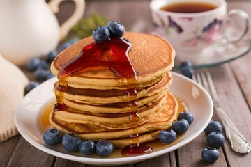 Pumpkin pancakes in high stack with blueberries and syrup served with tea in a rustic setting