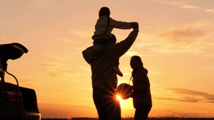 Silhouettes of family playing running at sunset near car, automobile. Man and woman running in circle, girl sitting on father's shoulders. Genuine joy, boundless fun in nature at setting evening sun. - obrazy, fototapety, plakaty