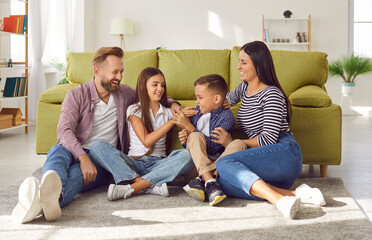 Portrait of happy laughing kids boy and girl having fun with their parents, sitting on the floor at home. Portrait of young couple family spending time together with children. Family leisure concept. - 787335411