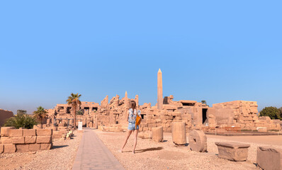 A beautiful young girl in mini shorts is standing examining historical artifacts - Ancient Temple of Karnak in Luxor - Ruined Thebes Egypt - obrazy, fototapety, plakaty