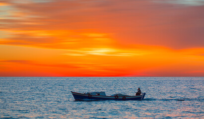 A fisherman departs Alanya Harbor on the Mediterranean sea in Alanya peninsula in the background at dusk - Alanya, Turkey 