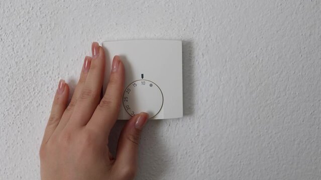 Human hand turns off the heating at home. Central Heating thermostat control dial adjustment. Place for text. Woman turning down heating thermostat to save money.