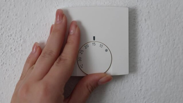 Woman lowers the temperature on the thermostat from 20 degrees Celsius to 15 degrees Celsius. Woman turning down heating thermostat to save money.