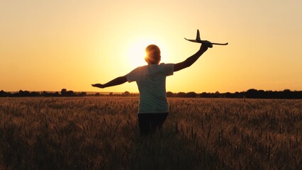 Cheerful boy teen running with plane toy on autumn wheat field at cinematic sunset sunrise back view closeup. Active male kid playing flying airplane plaything enjoy freedom happy childhood at meadow - obrazy, fototapety, plakaty