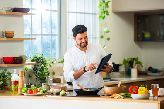 Indian asian bearded man cooking food in kitchen referring recipe from internet
