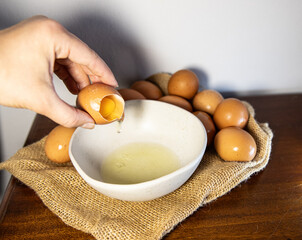A hand holds a broken egg. Separating the white from the yolk, background with chicken eggs for a recipe