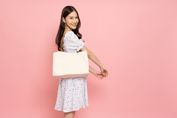 Happy Asian woman holding white textile eco bag or cloth bag isolated on pink background, Ecology or environment protection concept