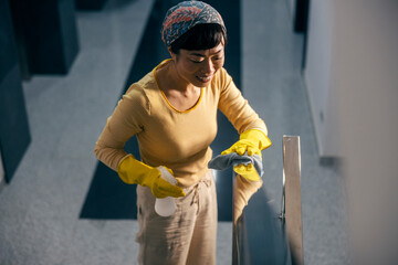 A tidy Japanese housekeeper is cleaning railing in building hall.