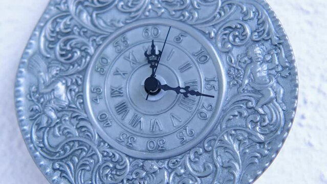 vintage silver clock of 19th century on white wall counts down the time, the hands move on dial, concept of road of life, time goes by, an irreversible flow from past, through present to future
