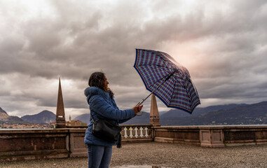 beautiful middle aged woman opening umbrella on the terrace of Borromeo palace on Isola Bella in the rain splashing water drops